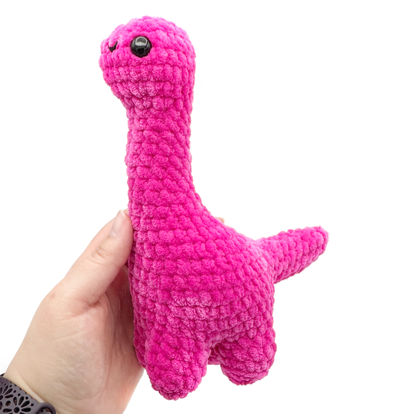 Crochet amigurumi brontosaurus plushie in hot pink held in hand