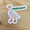Die cut glossy vinyl sticker with a white goose that says "menace" on wood background