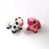 Two 3D printed cow mini fidget creatures - one in black and white, the other is a pink strawberry cow