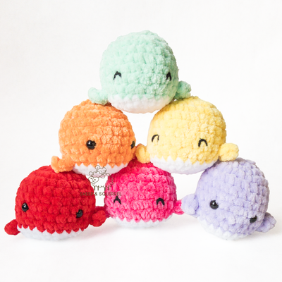 Six little amigurumi crochet stuffed animal whales in an assortment of colors stacked in a pyramid