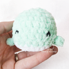 Front view of a little amigurumi crochet stuffed animal whale being held in hand featuring embroidered smiling eyes