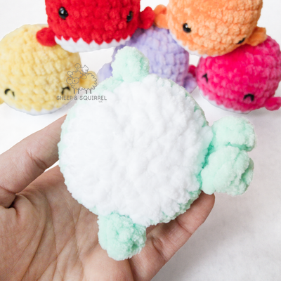 Bottom view of a little amigurumi crochet stuffed animal whale being held in hand, with 5 other little whales in the background