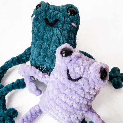 Two crochet amigurumi leggy frogs sitting