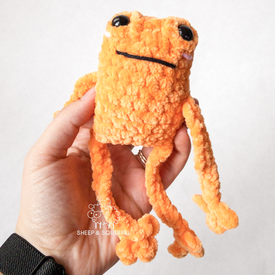 One crochet amigurumi leggy frog being held with arms and legs dangling